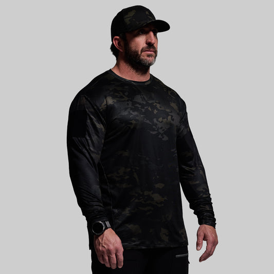 Man wearing a black long-sleeve camouflage shirt and cap on a gray background