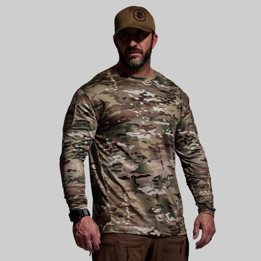Man wearing a camouflage long-sleeve shirt and brown cap on a gray background