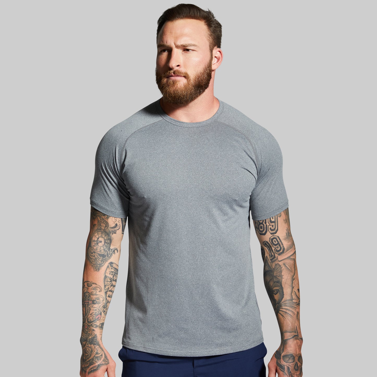 Man wearing a gray t-shirt with tattoos on arms against a gray background