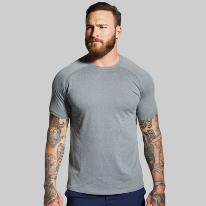 Man wearing a gray t-shirt with tattoos on arms against a gray background