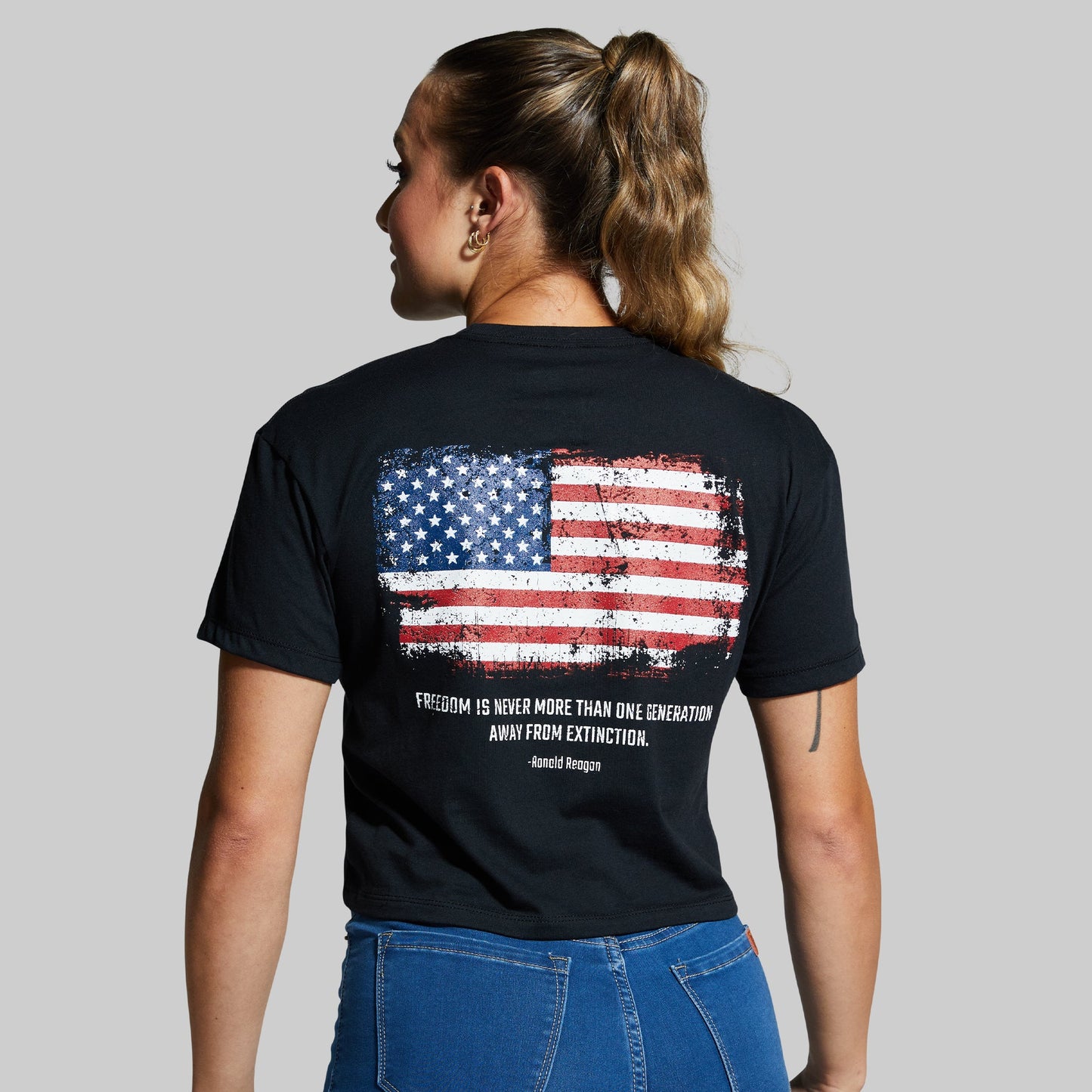 Person wearing a black t-shirt with an American flag design on the back against a gray background