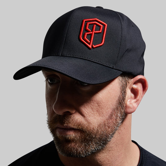 Man wearing a black cap with a red logo on a gray background