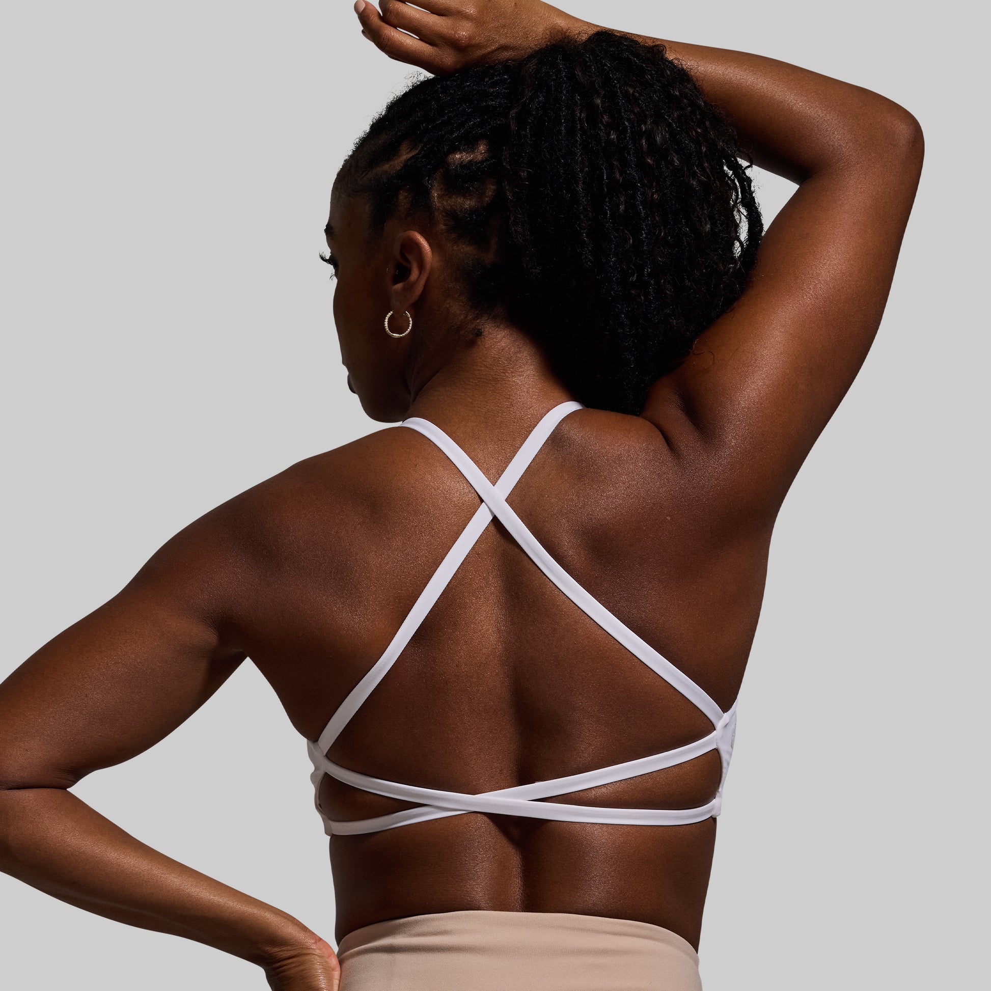 Woman wearing a white strappy sports bra against a gray background