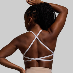 Woman wearing a white strappy sports bra against a gray background