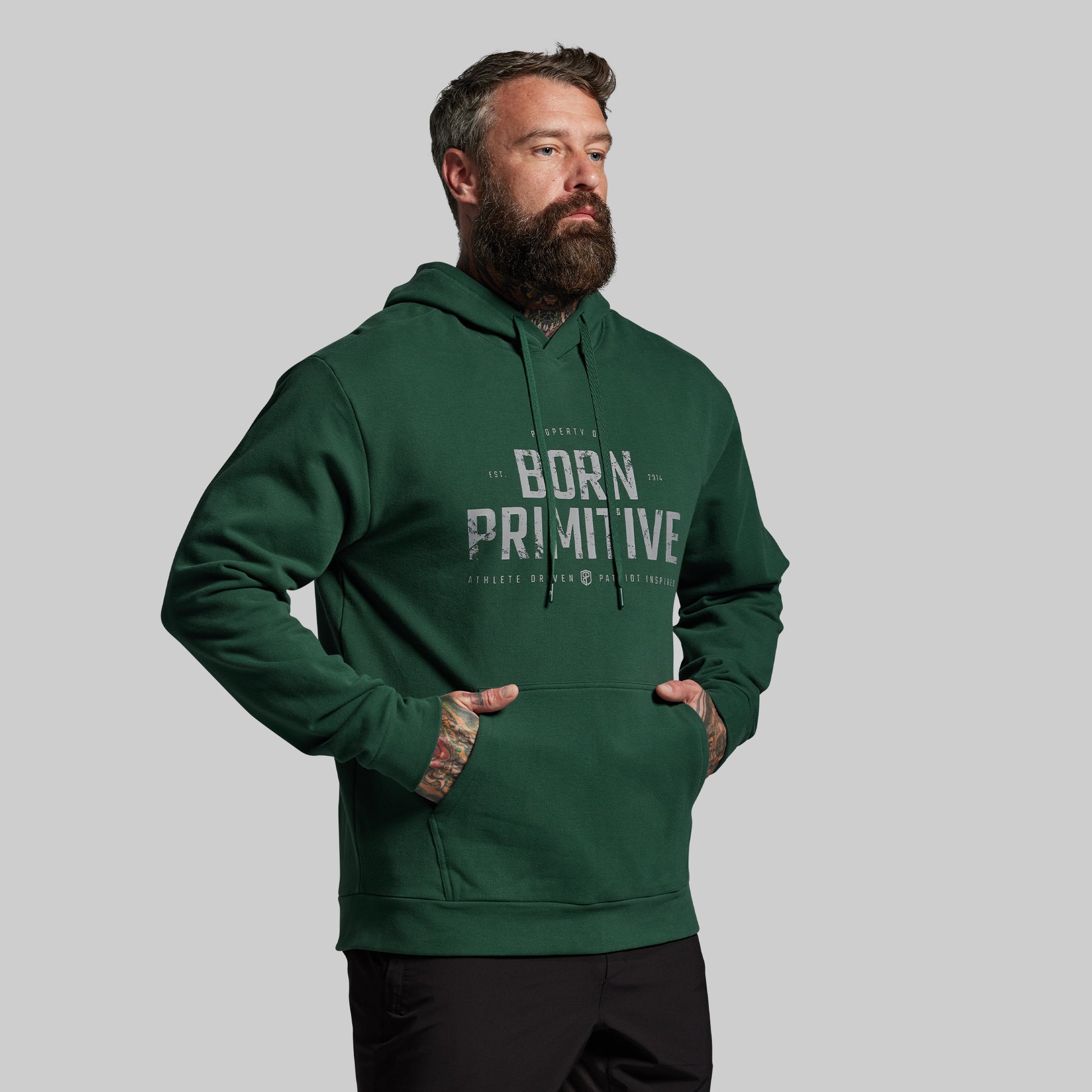 Man wearing a green hoodie with 'Born Primitive' text on a gray background