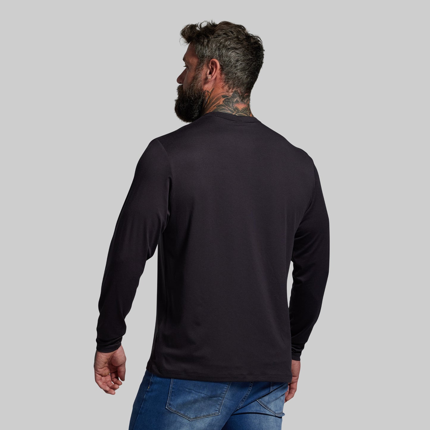 Man wearing a black long-sleeve shirt and blue jeans on a gray background