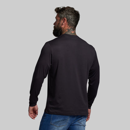 Man wearing a black long-sleeve shirt and blue jeans on a gray background