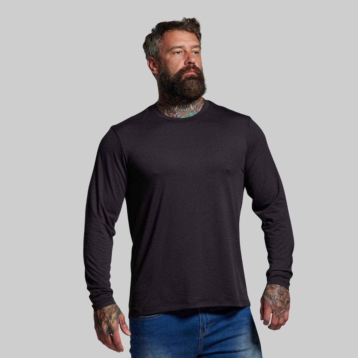 Man wearing a black long-sleeve shirt and blue jeans against a gray background