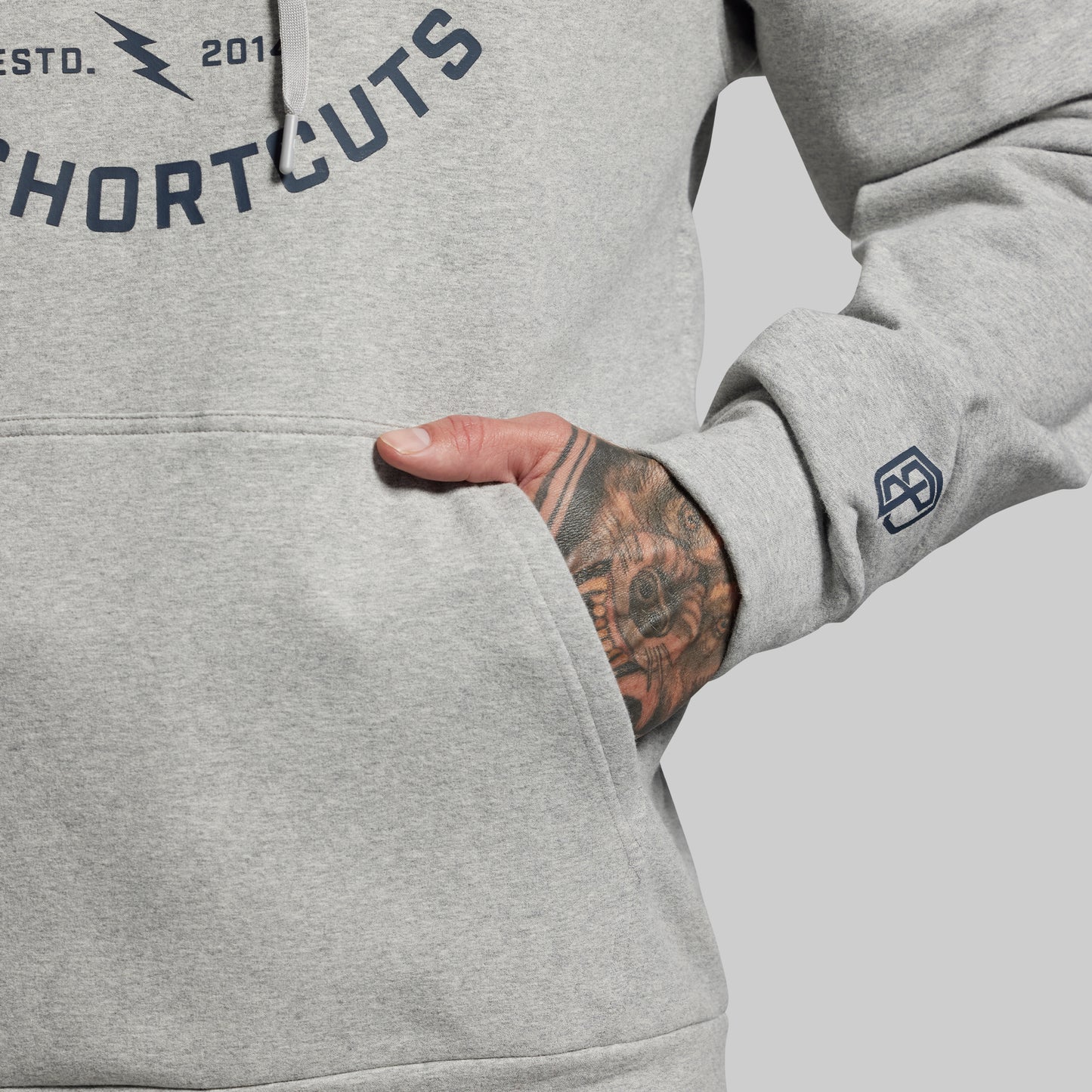 Close-up of gray hoodie with hand in pocket and tattooed arm on a light gray background