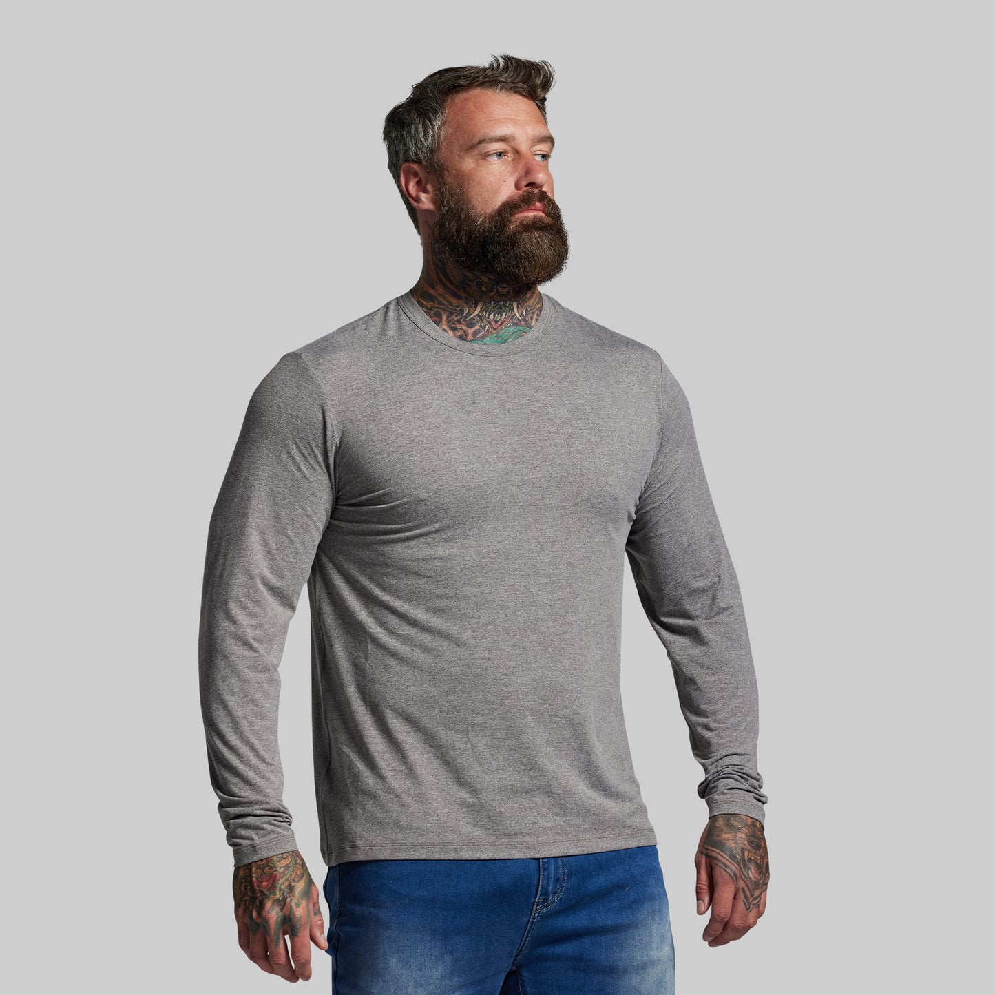 Man wearing a gray long-sleeve shirt and blue jeans against a plain background