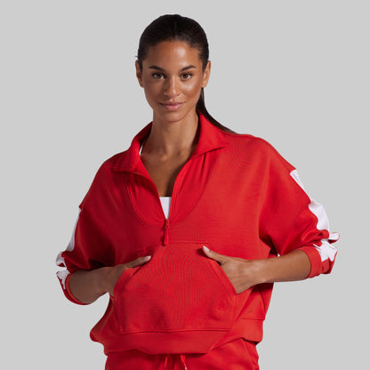 A woman modeling a bright red athletic zip-up jacket with white sleeve stripes, posed against a solid light gray background.