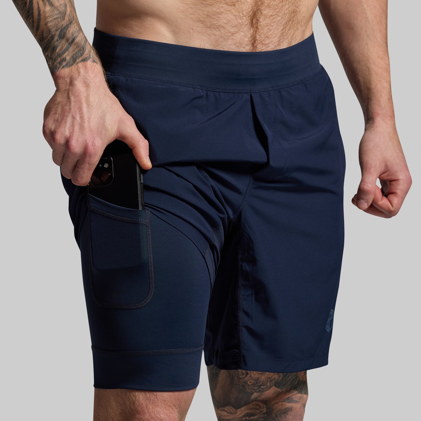 A man wearing navy blue athletic shorts with pockets and a visible mobile phone in one of the pockets.