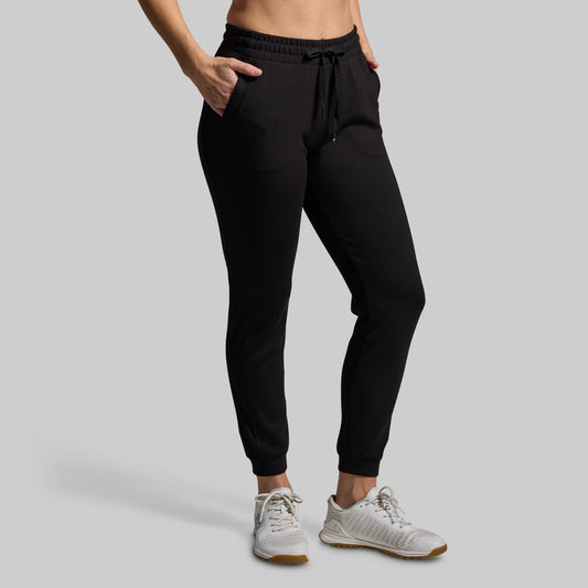 Person wearing black jogger pants and white sneakers on a gray background