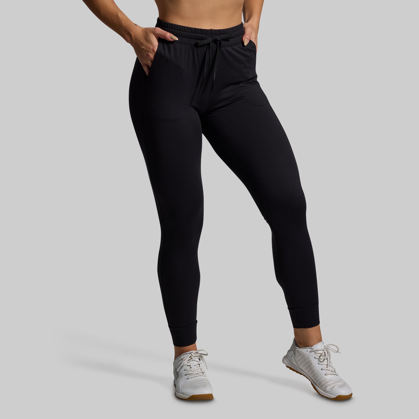 Person wearing black joggers and white sneakers on a gray background