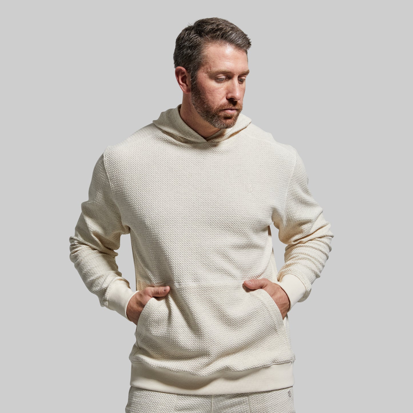 Man wearing a cream-colored textured hoodie against a plain background