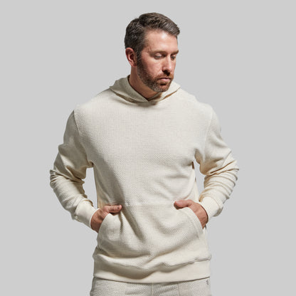 Man wearing a cream-colored textured hoodie against a plain background