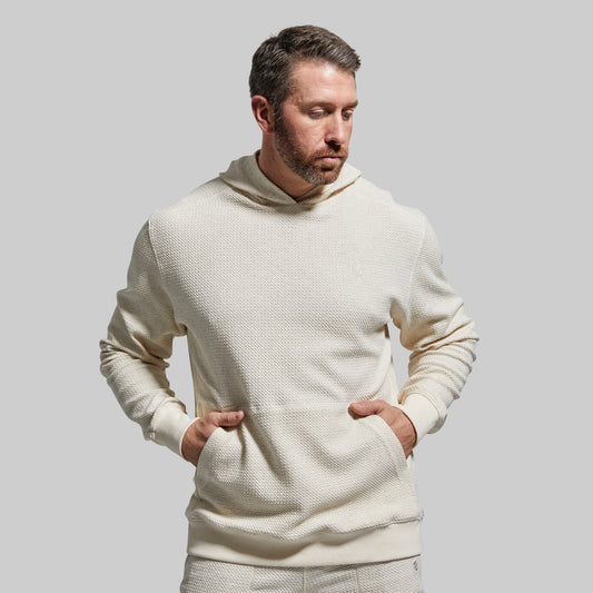 A man wearing a beige hooded sweatshirt with a waffle-textured material.