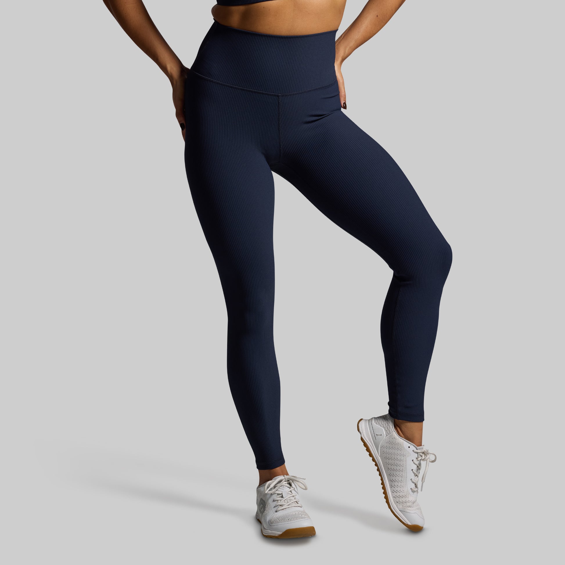 Person wearing navy leggings and white sneakers on a gray background