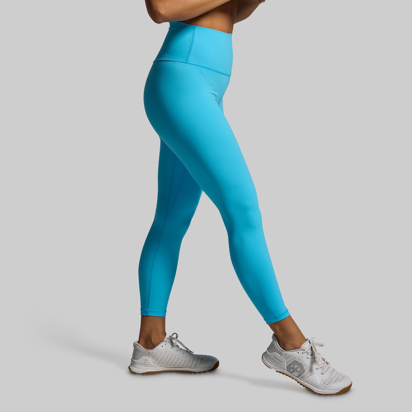 Person wearing bright blue leggings and white sneakers on a gray background