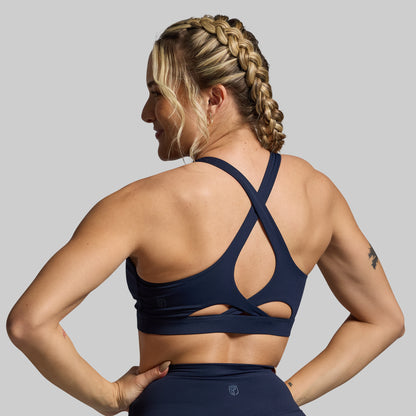 Woman wearing a navy blue sports bra and leggings on a gray background