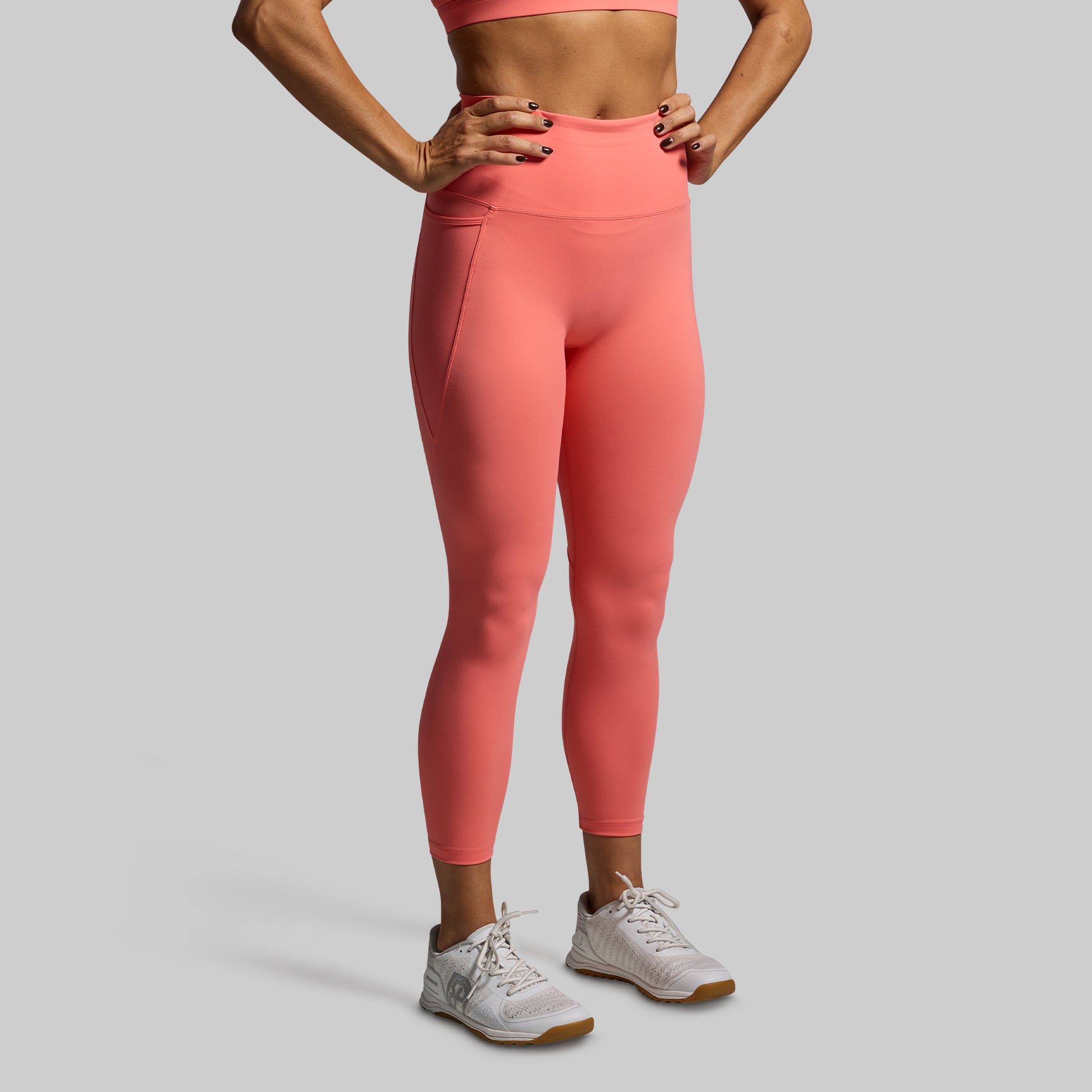 Person wearing coral leggings and a sports bra on a gray background