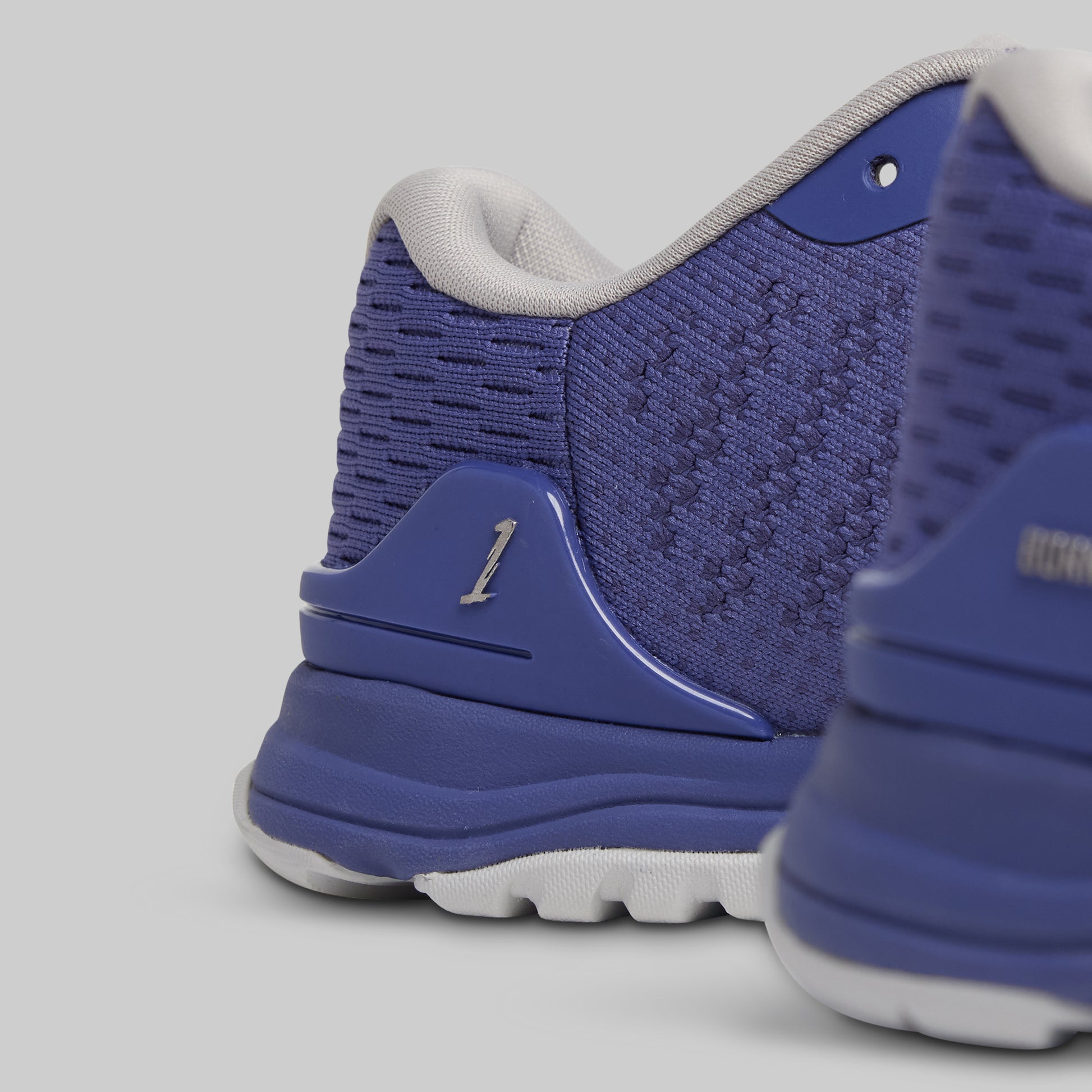 Blue athletic shoe with a white sole on a gray background
