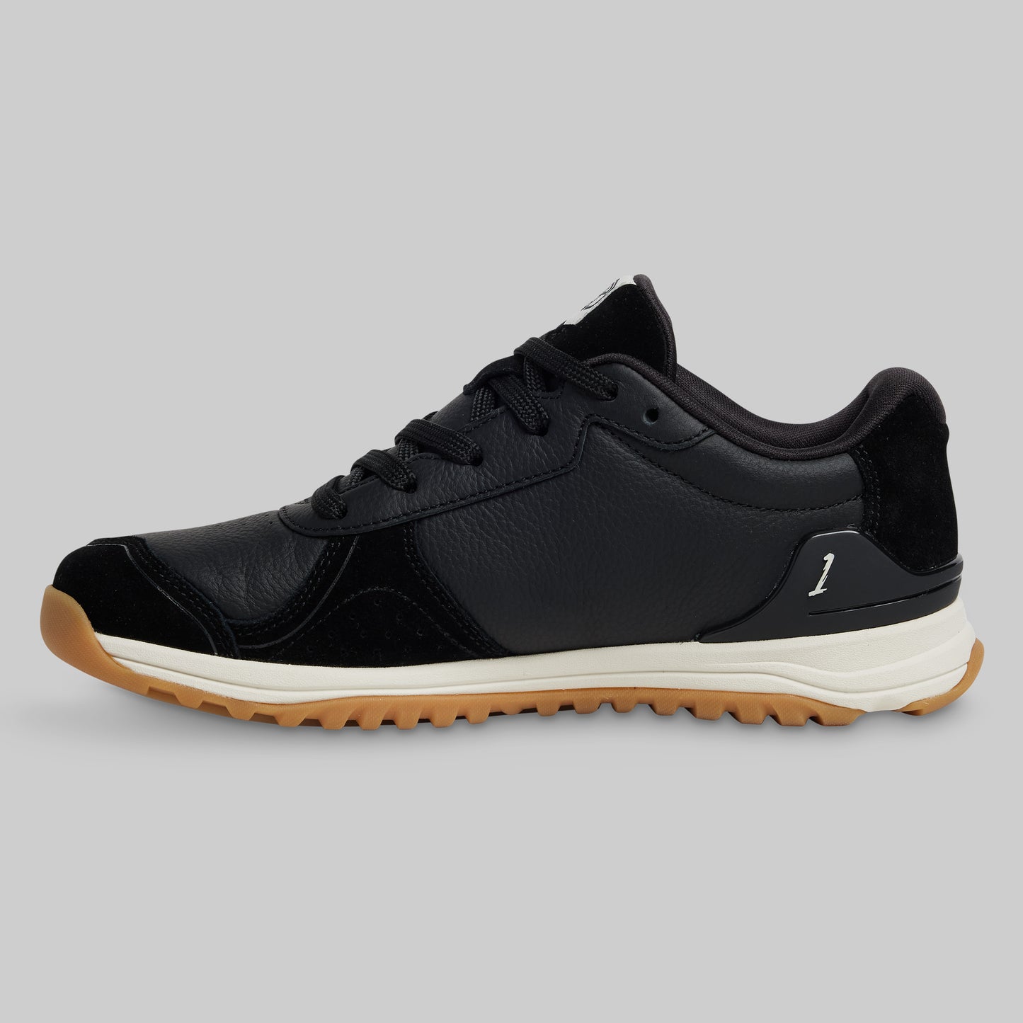 Black sneaker with a brown sole on a gray background