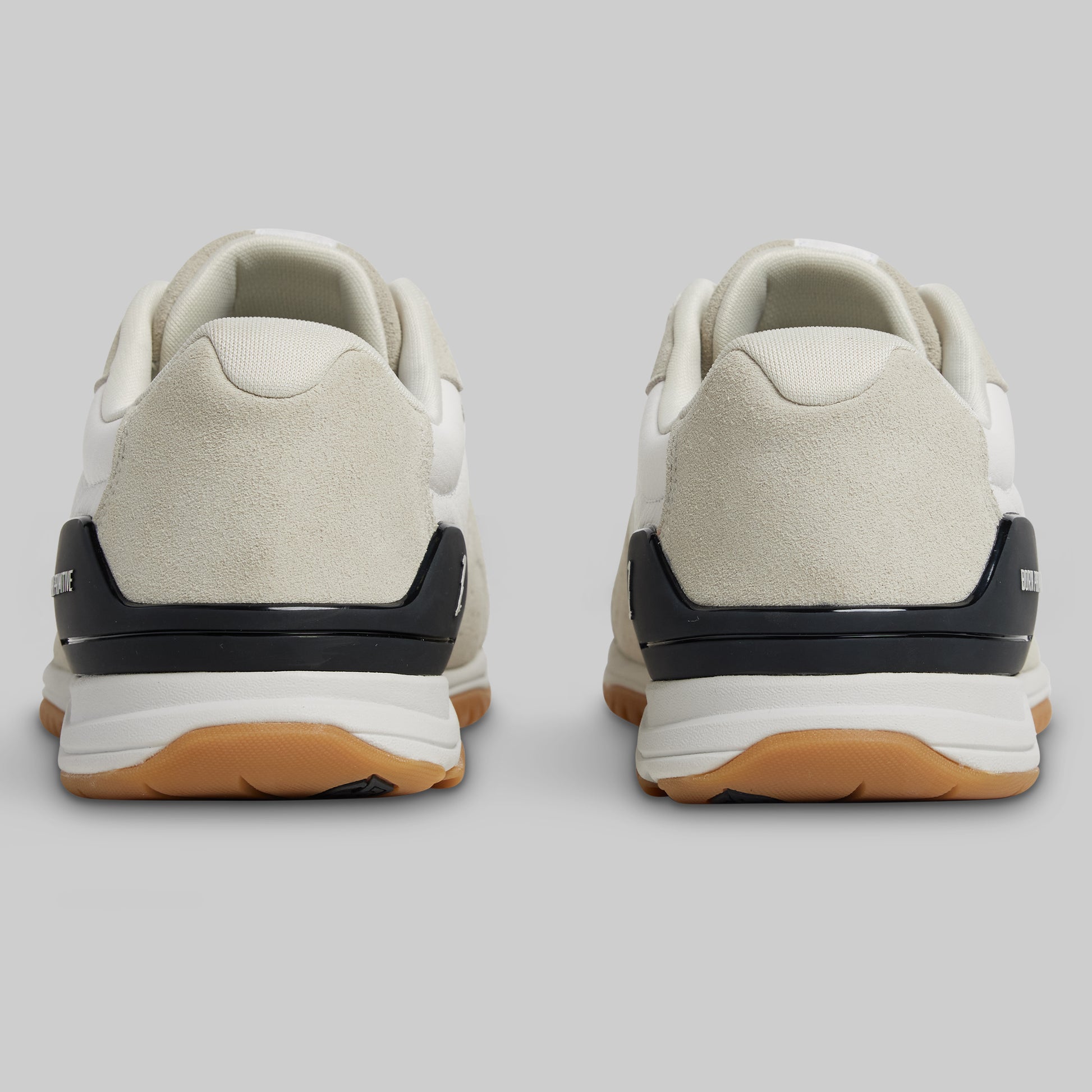 Pair of beige sneakers with black and brown accents on a light gray background