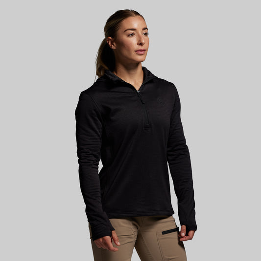 Woman wearing a black long-sleeve shirt with a hood against a gray background