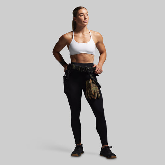 Woman wearing a white sports bra and black leggings with tactical pouches on a gray background
