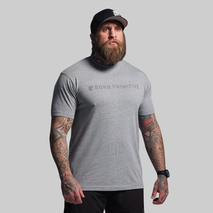 Man wearing a gray 'Born Primitive' t-shirt and black cap on a light gray background