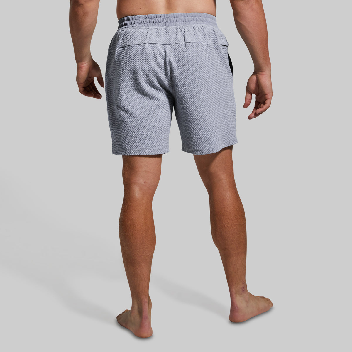 Rear view of a man wearing light gray textured shorts against a solid light gray background.