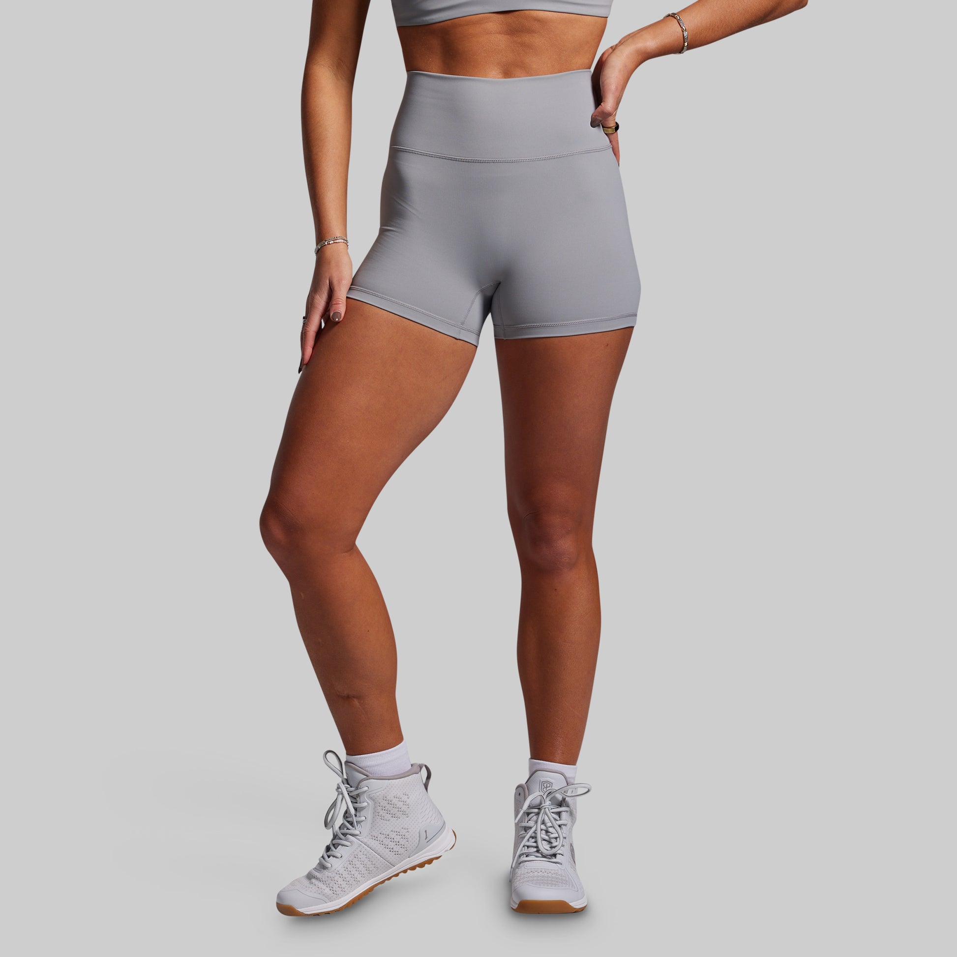 Person wearing gray athletic shorts and white sneakers on a plain background