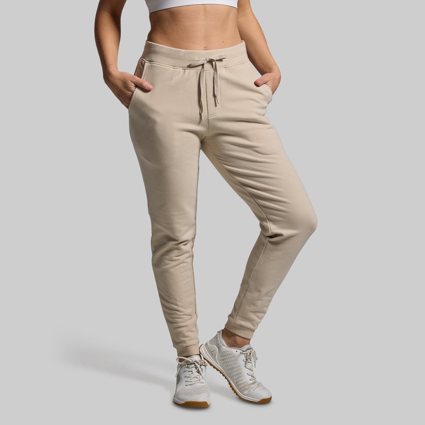 Beige jogger pants worn by a person on a gray background