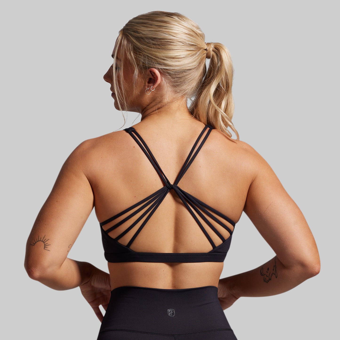 Woman wearing a black strappy sports bra and leggings on a gray background