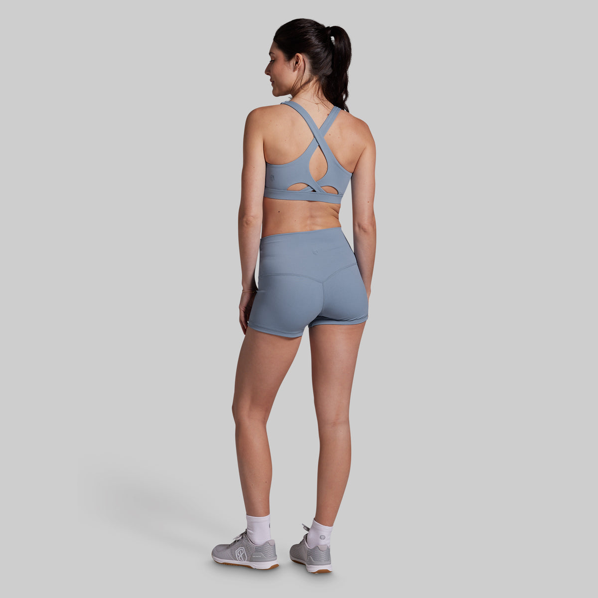 Woman wearing a gray sports bra and shorts set on a light gray background
