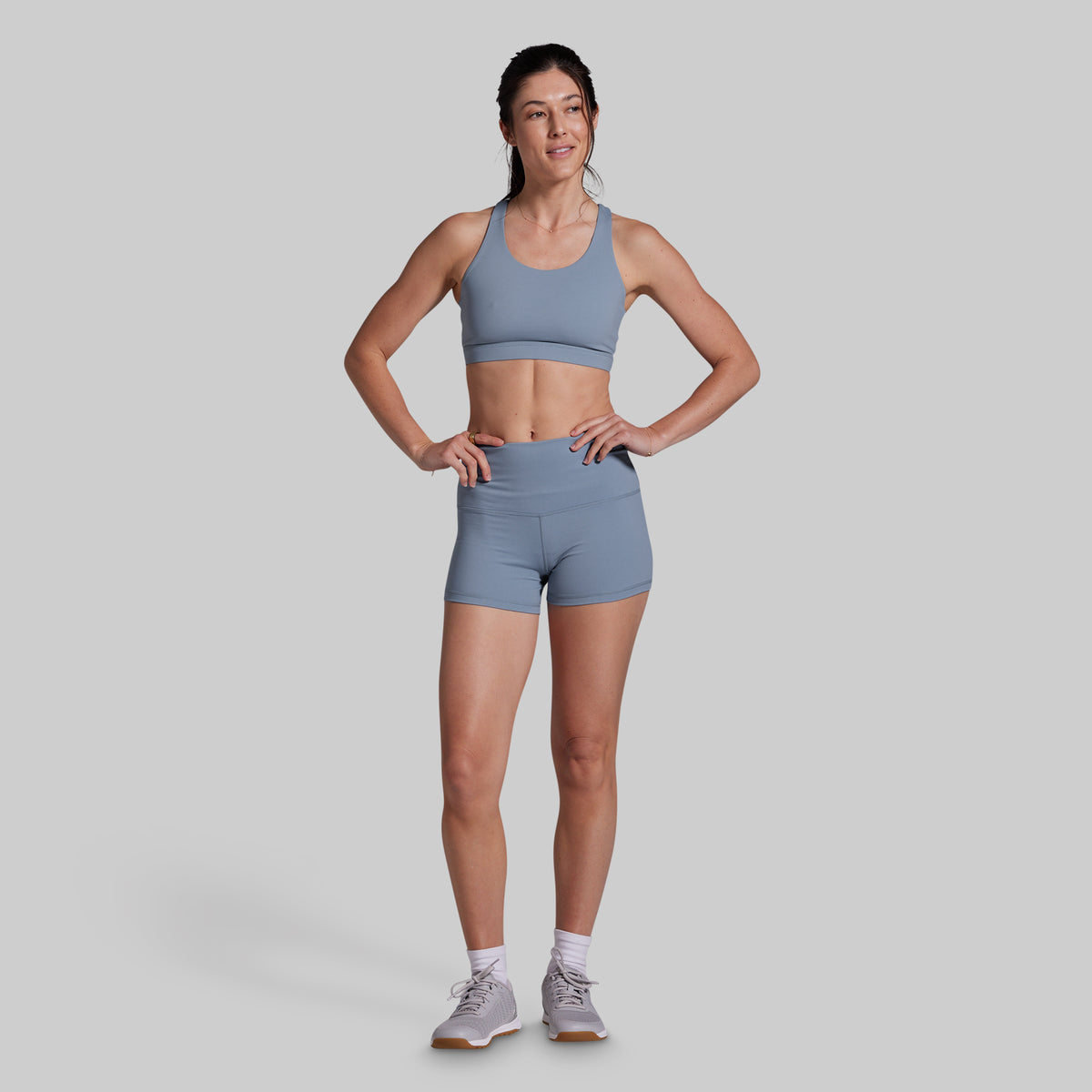 Woman wearing a gray sports bra and shorts on a light gray background