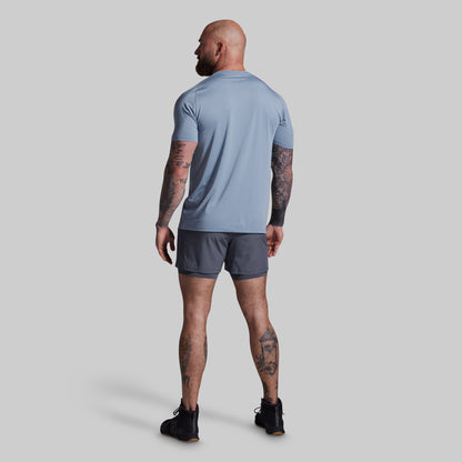 Man wearing a light blue t-shirt and gray shorts on a plain background