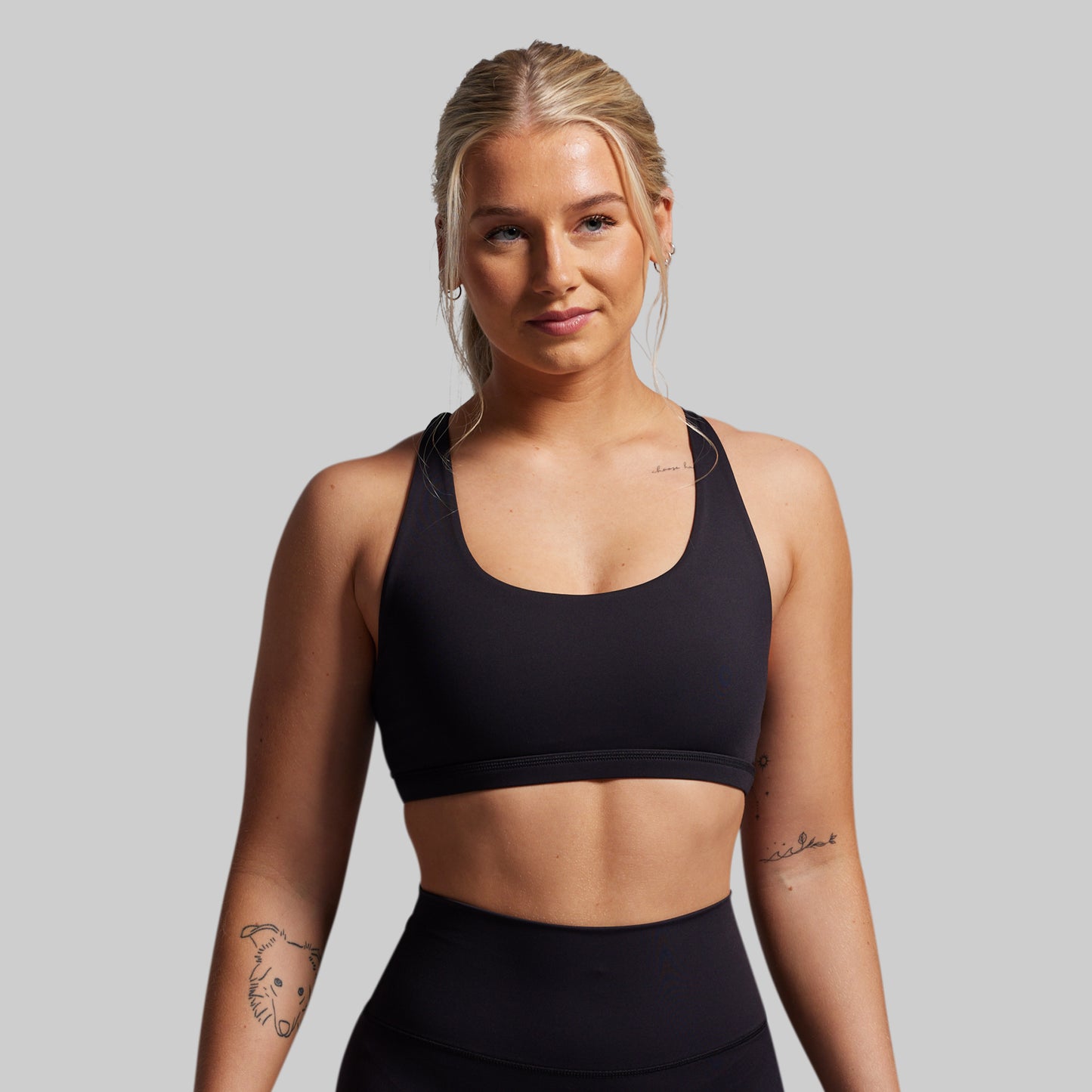 Woman wearing a black sports bra and leggings on a gray background
