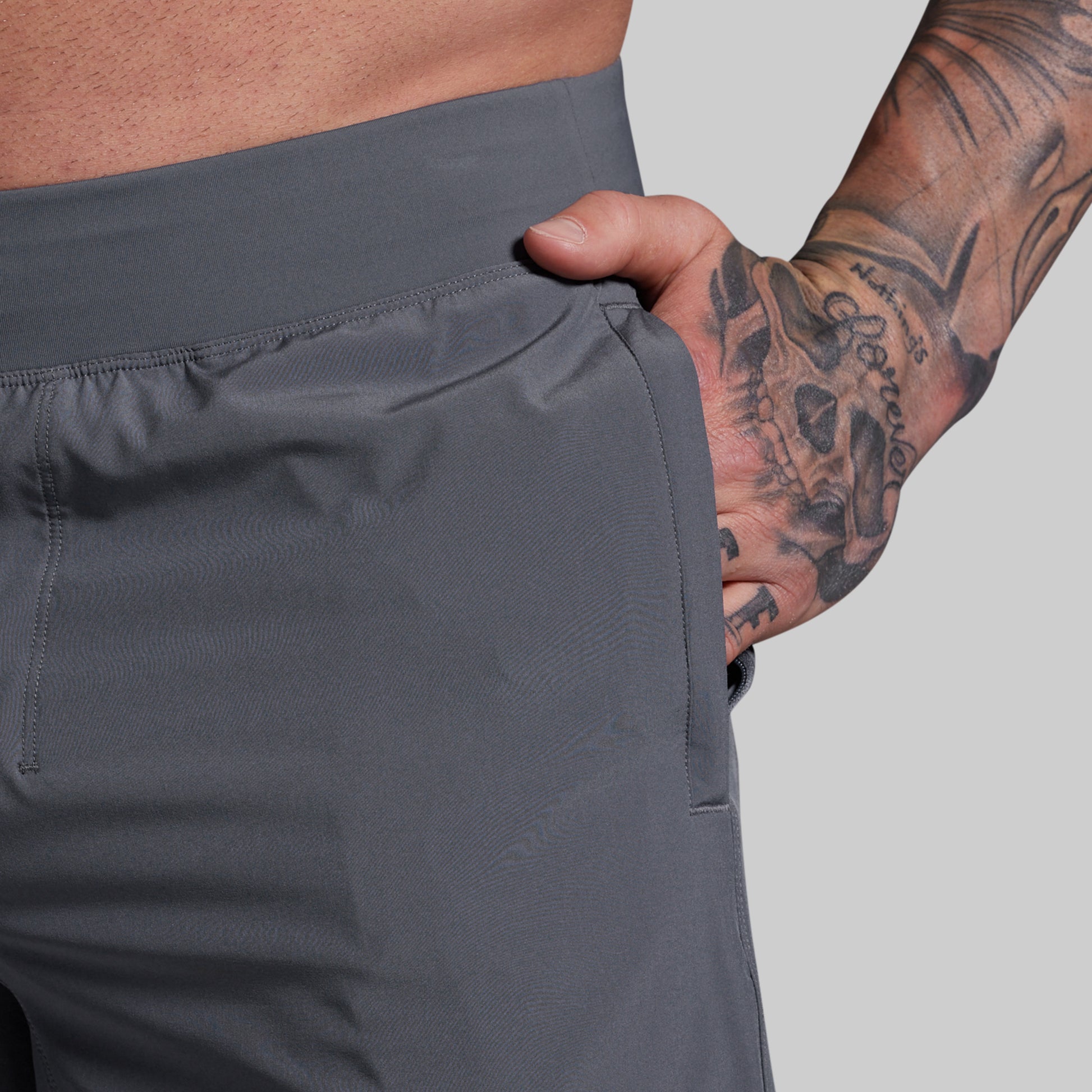 Person wearing gray shorts with a tattooed arm on a light gray background