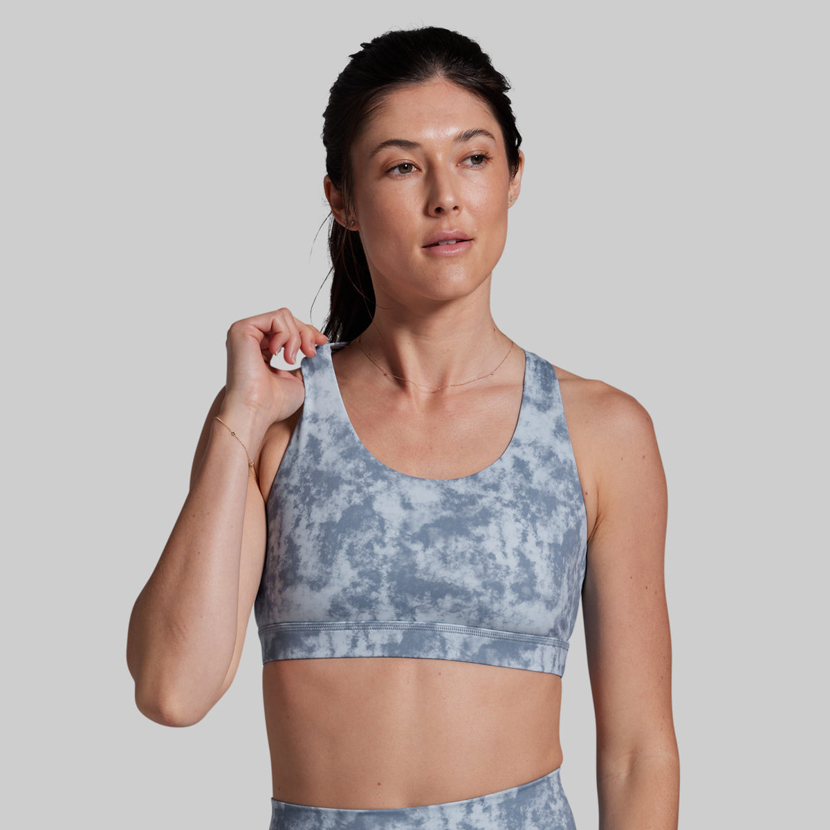 Woman wearing a blue tie-dye sports bra and leggings on a plain background