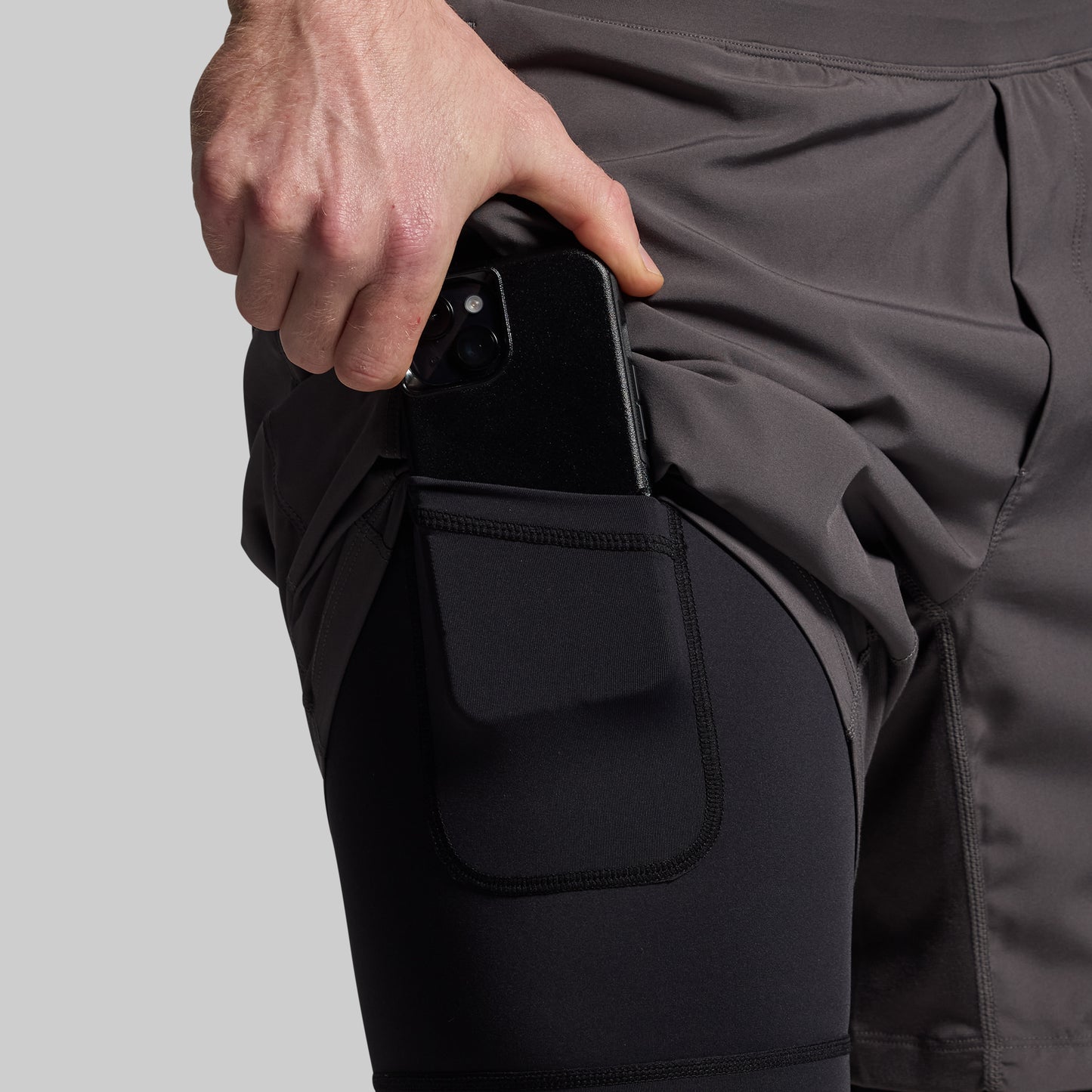 A person wearing gray versatile shorts with a compression liner and a phone held in the pocket.
