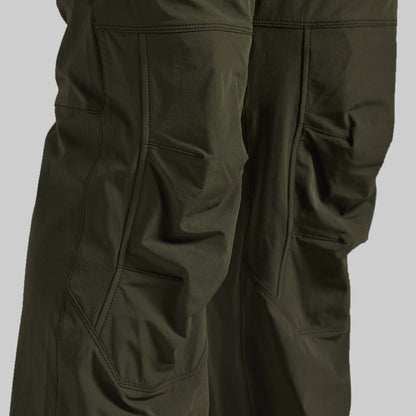 Close-up of dark olive green outdoor pants showing the fabric texture, seams, and side pockets against a neutral gray background.