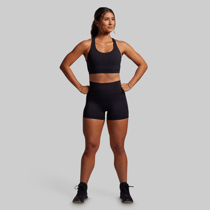 Woman wearing a black sports bra and shorts on a gray background