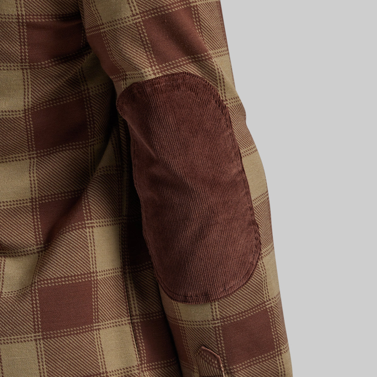 Close-up of a brown and beige plaid jacket or shirt sleeve with a brown corduroy elbow patch on a light gray background.