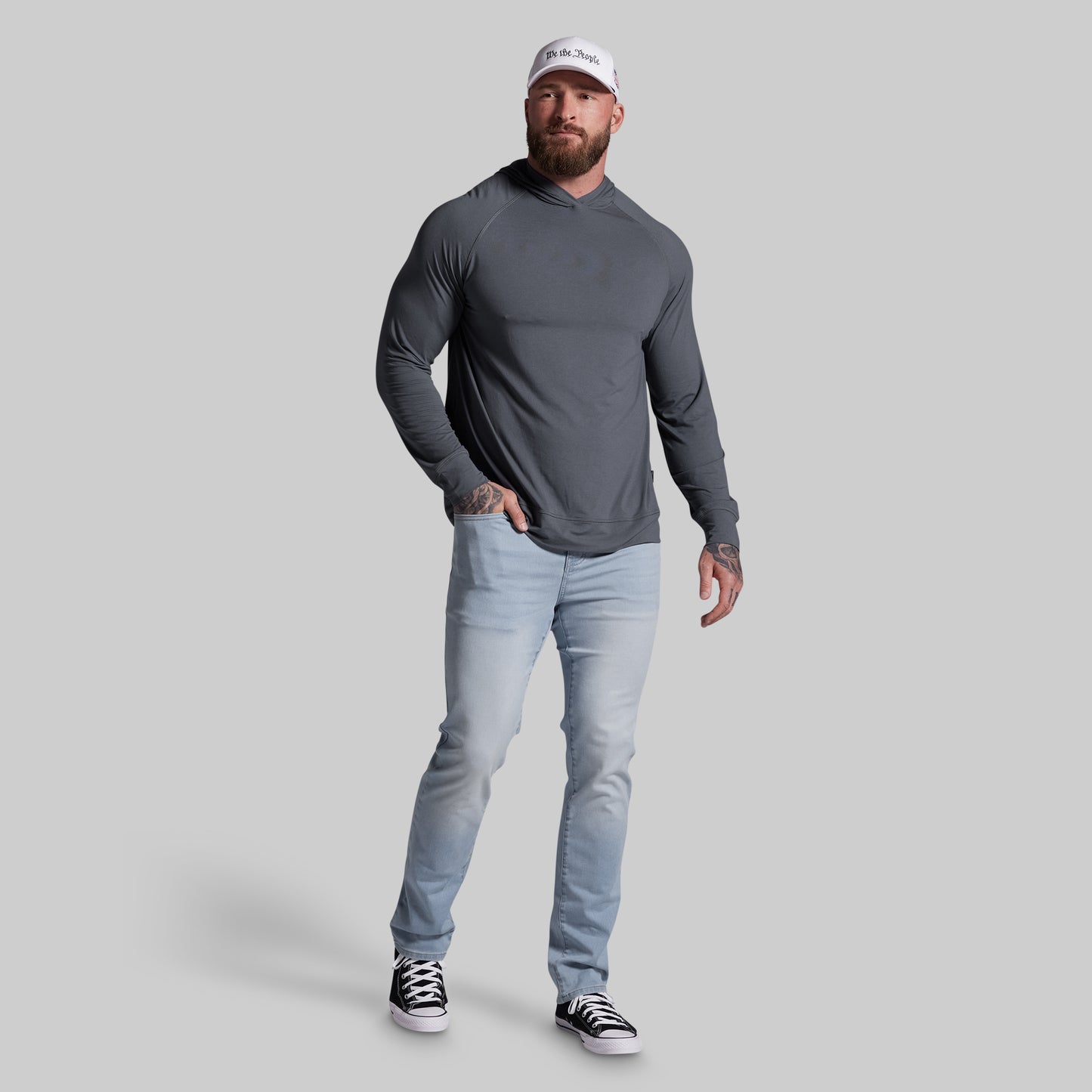 Man wearing a gray long-sleeve shirt, light blue jeans, and black sneakers on a gray background