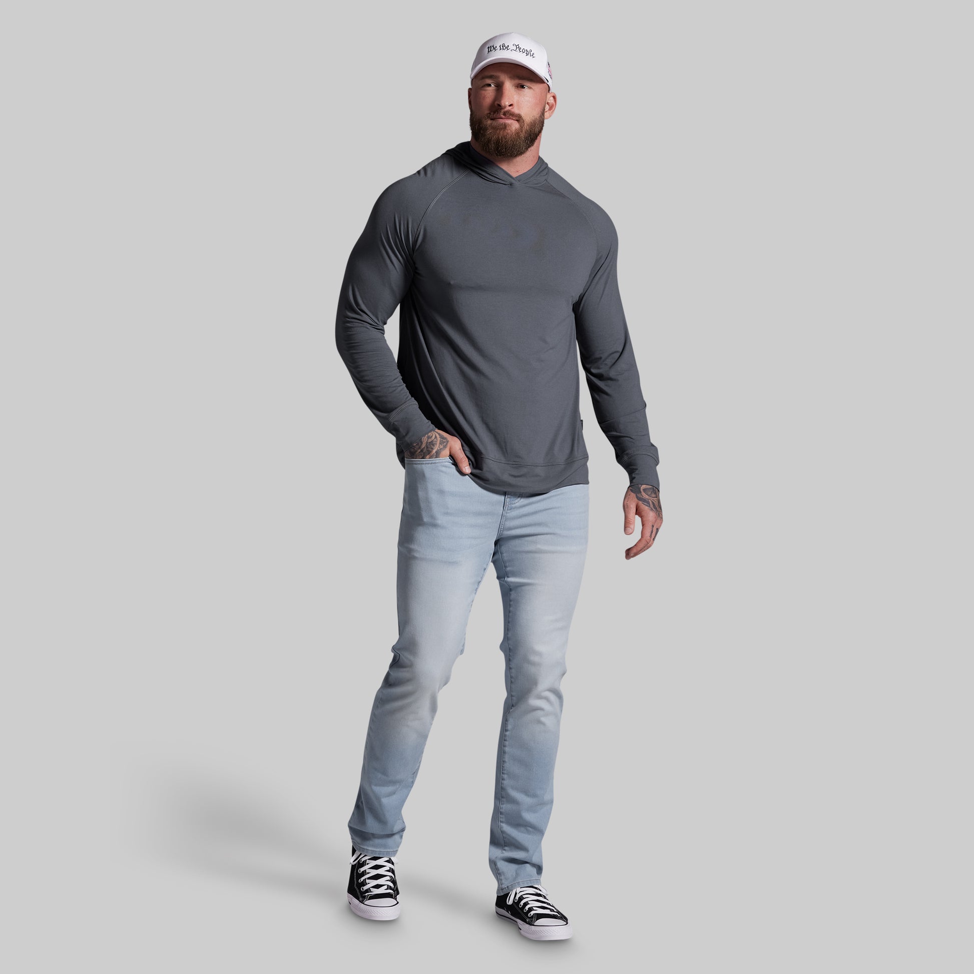 Man wearing a gray long-sleeve shirt, light blue jeans, and black sneakers on a gray background