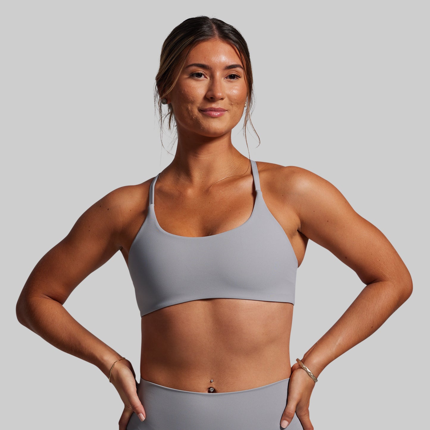Woman wearing a gray sports bra and leggings on a plain background