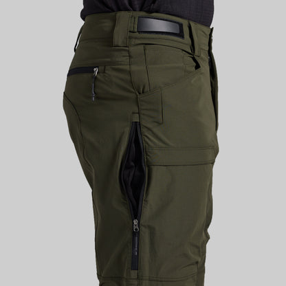 Close-up of olive green cargo pants with multiple zippered pockets, shown on a model from the waist down against a light gray background.