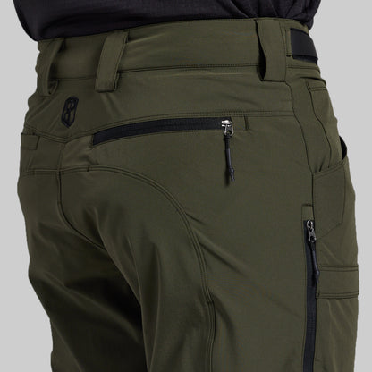 Close-up of the back waist and pockets of olive green technical outdoor pants, showing a zippered pocket, belt loops, and a small black logo patch.